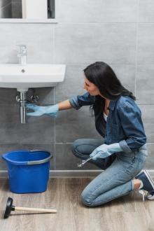 Woman with dark hair and rubber gloves trying to fix leaking bathroom sink