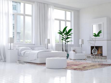 Bedroom with two green plants and an all-white bed, chair, walls, and floors 