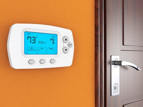 Digital thermostat on orange wall next to wooden door Digital thermostat on orange wall next to wooden door
