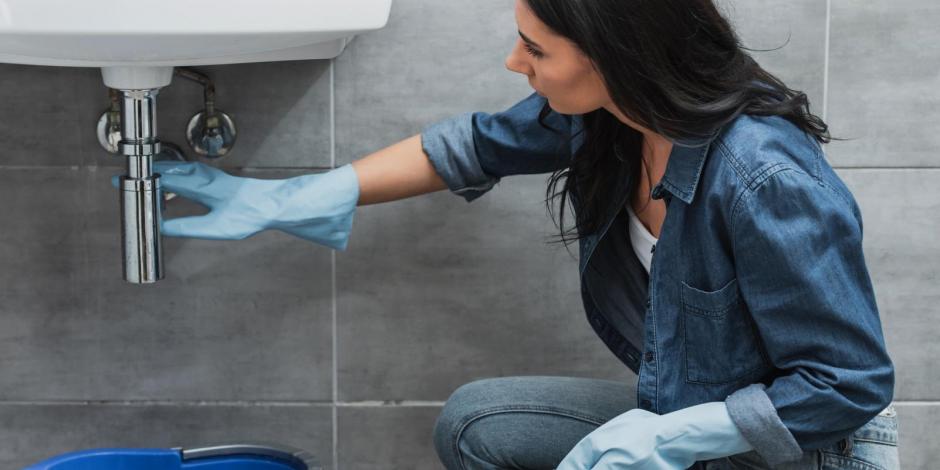 Woman with dark hair and rubber gloves trying to fix leaking bathroom sink