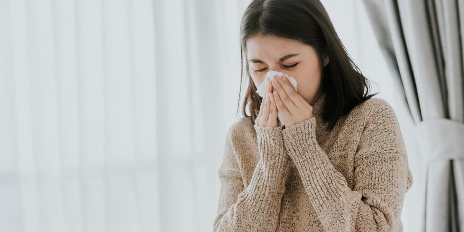 Woman sneezing into tissue while sick at home Woman sneezing into tissue while sick at home
