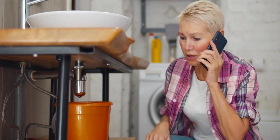 Woman calling plumber having water leaking from sink pipe