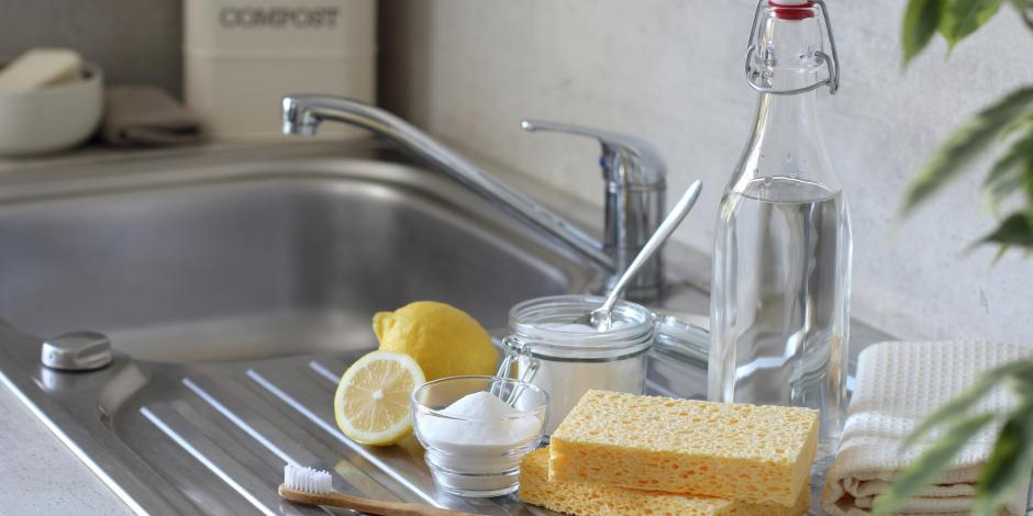 Cleaning solutions next to sink like lemon, baking soda, toothbrush, and sponges