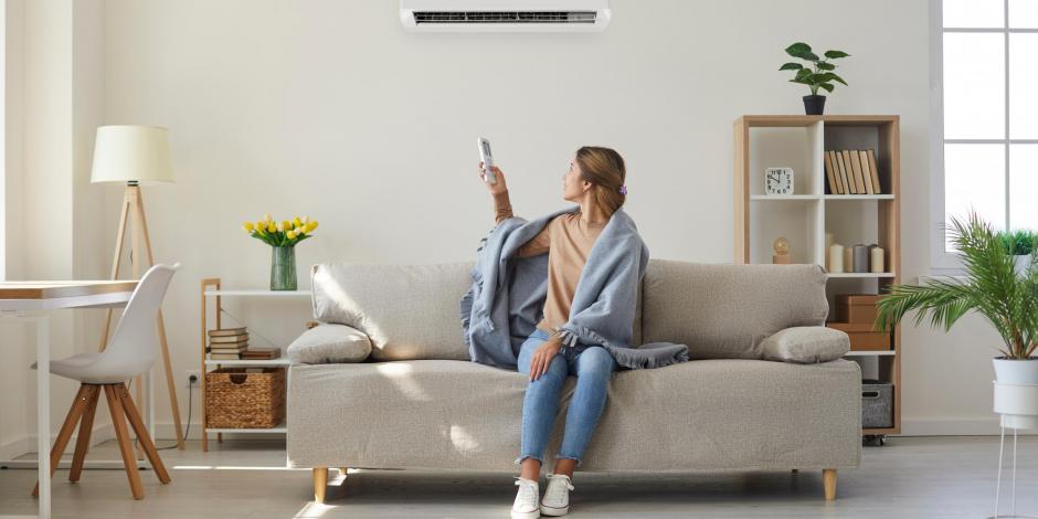 Woman controlling heat pump with a remote control from her couch