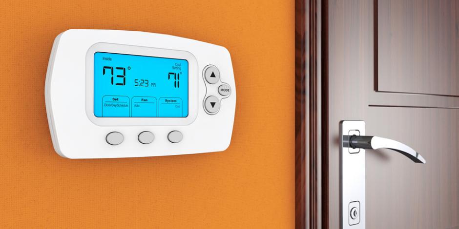 Digital thermostat on orange wall next to wooden door Digital thermostat on orange wall next to wooden door