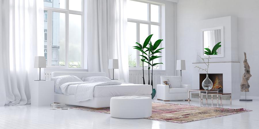 Bedroom with two green plants and an all-white bed, chair, walls, and floors 